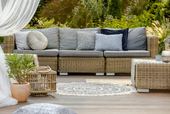 Geflochtene Gartenmöbel mit grauen Kissen auf einer Terrasse.